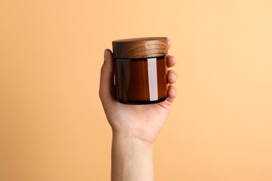 Photo of Woman holding jar of face cream on coral background, closeup