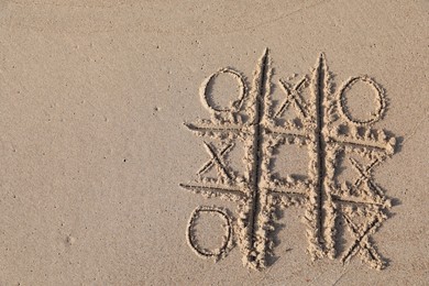Photo of Tic tac toe game drawn on sandy beach, top view. Space for text