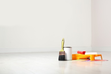 Can of paint and decorator tools on wooden floor indoors. Space for text