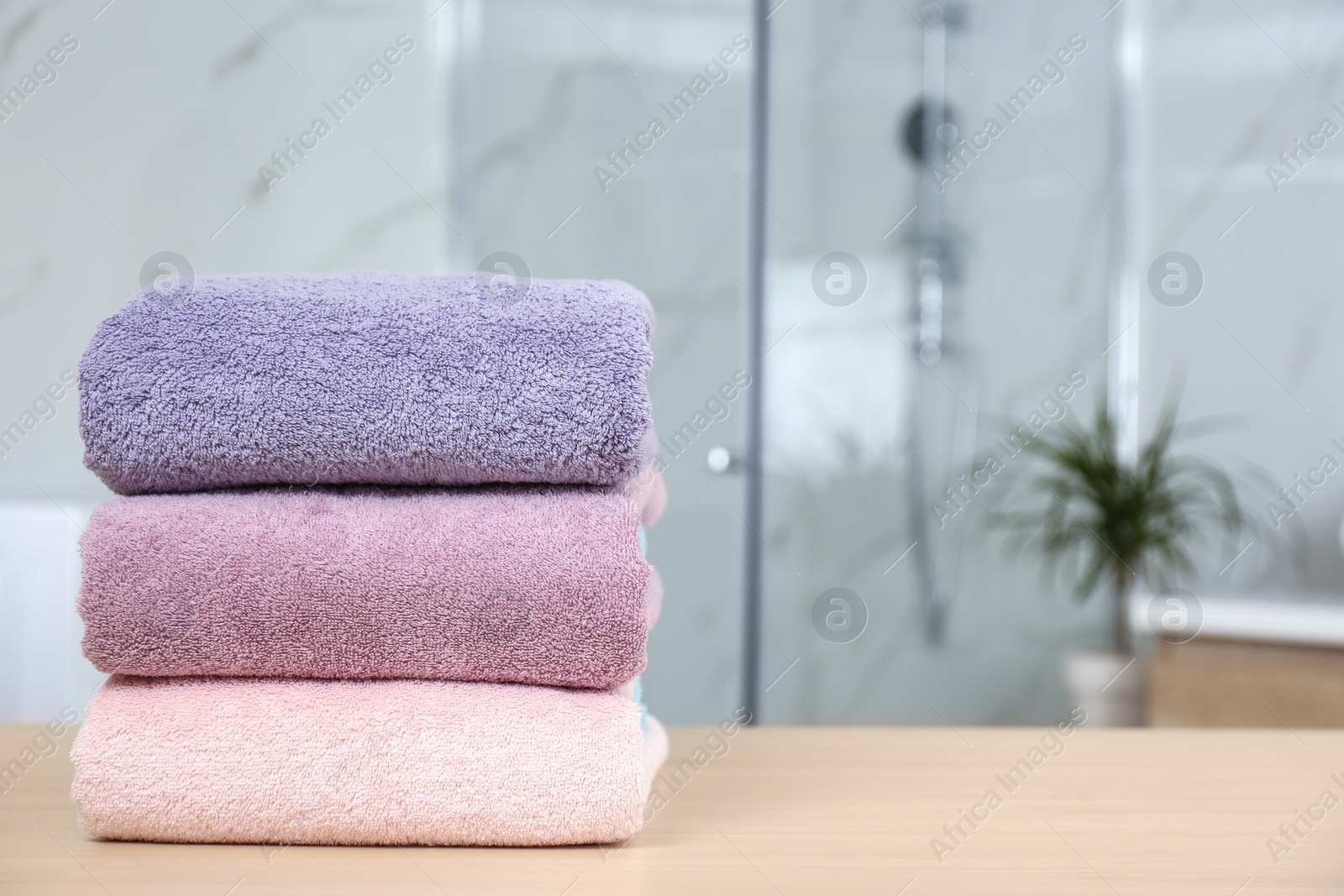 Photo of Stack of fresh towels on wooden table in bathroom. Space for text