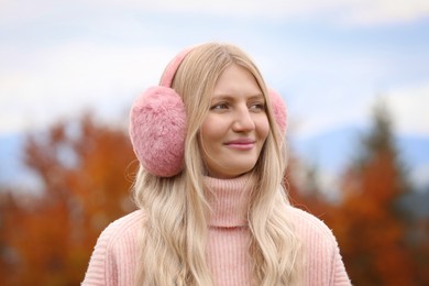 Photo of Young beautiful woman wearing warm earmuffs outdoors