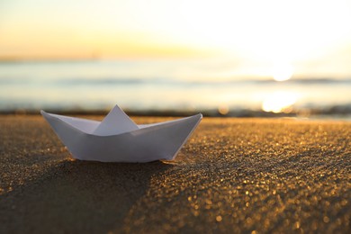 Photo of White paper boat on sand near sea at sunset. Space for text