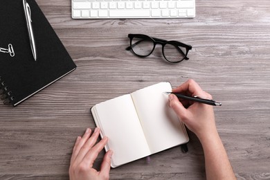 Photo of Woman writing in notebook at wooden table, top view