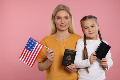 Immigration. Happy woman with her daughter holding passports and American flags on pink background