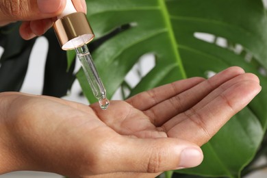 Woman applying cosmetic serum onto her hand near green plant, closeup