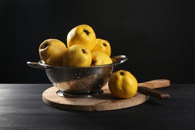 Photo of Tasty ripe quinces with water drops in metal colander and knife on black wooden table