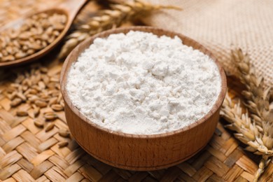 Wheat flour in wooden bowl and spikes on wicker mat, closeup