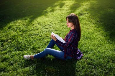 Young woman reading book on green grass outdoors