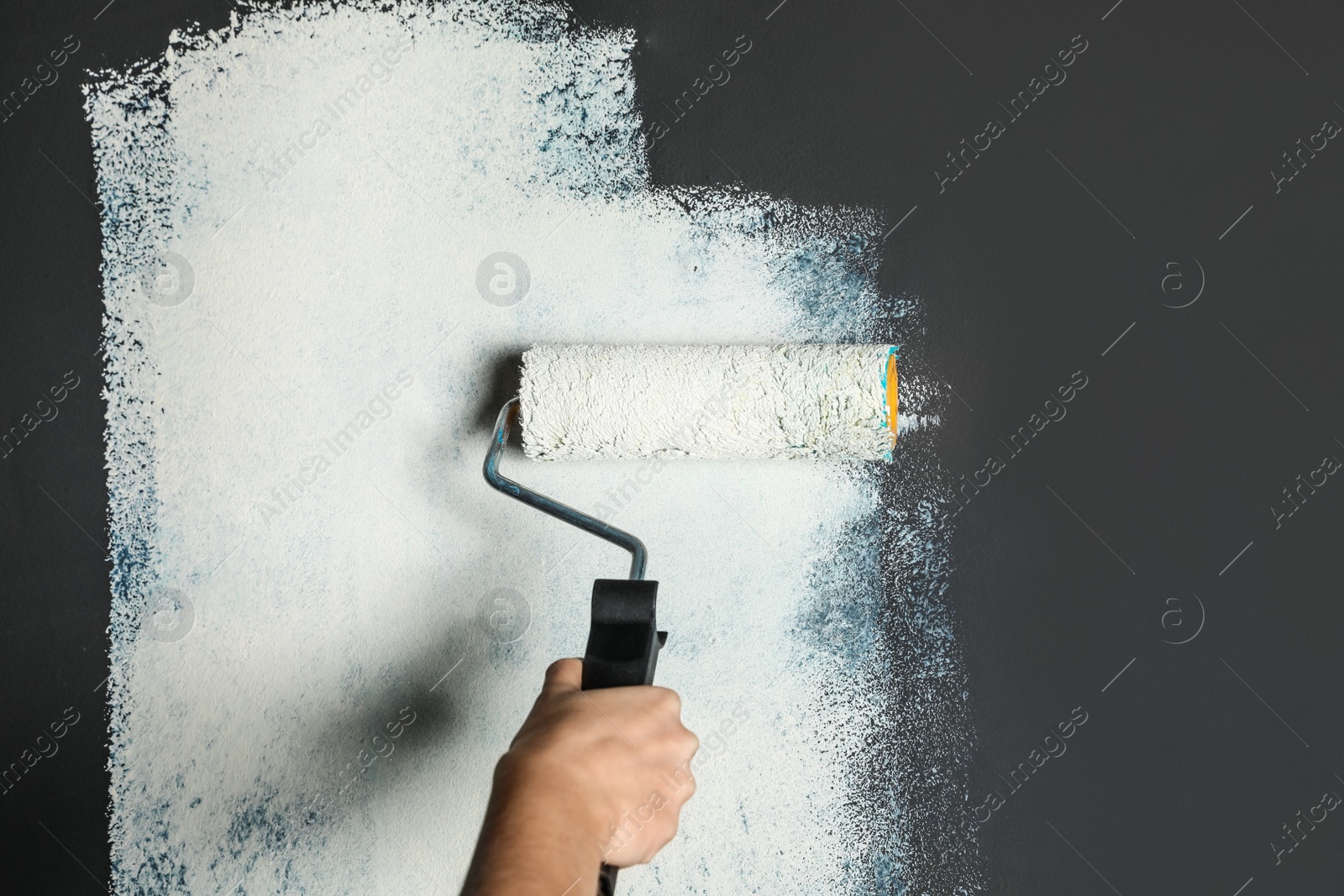 Photo of Woman painting grey wall with white dye, closeup