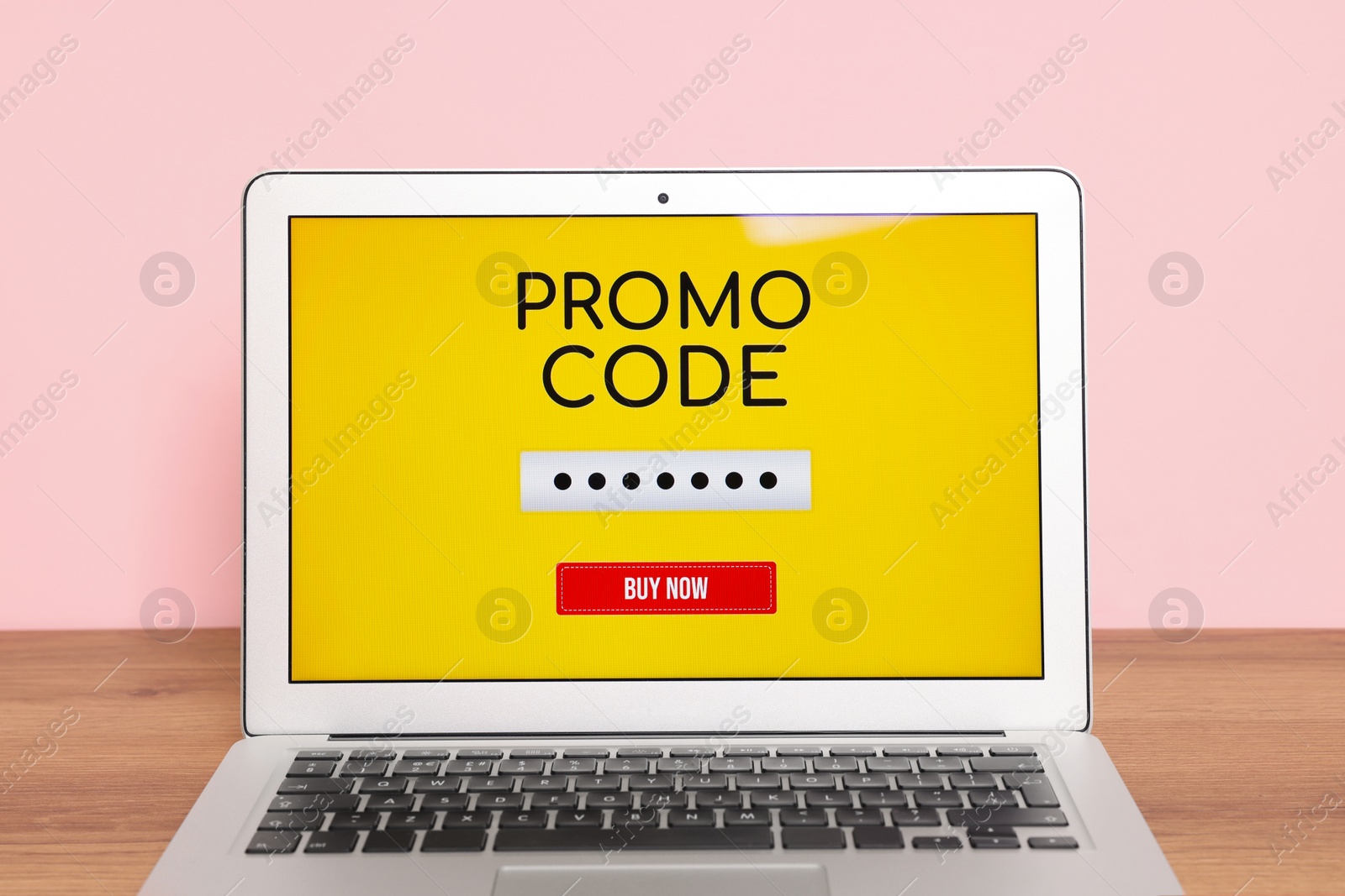 Photo of Laptop with activated promo code on wooden table near pink wall