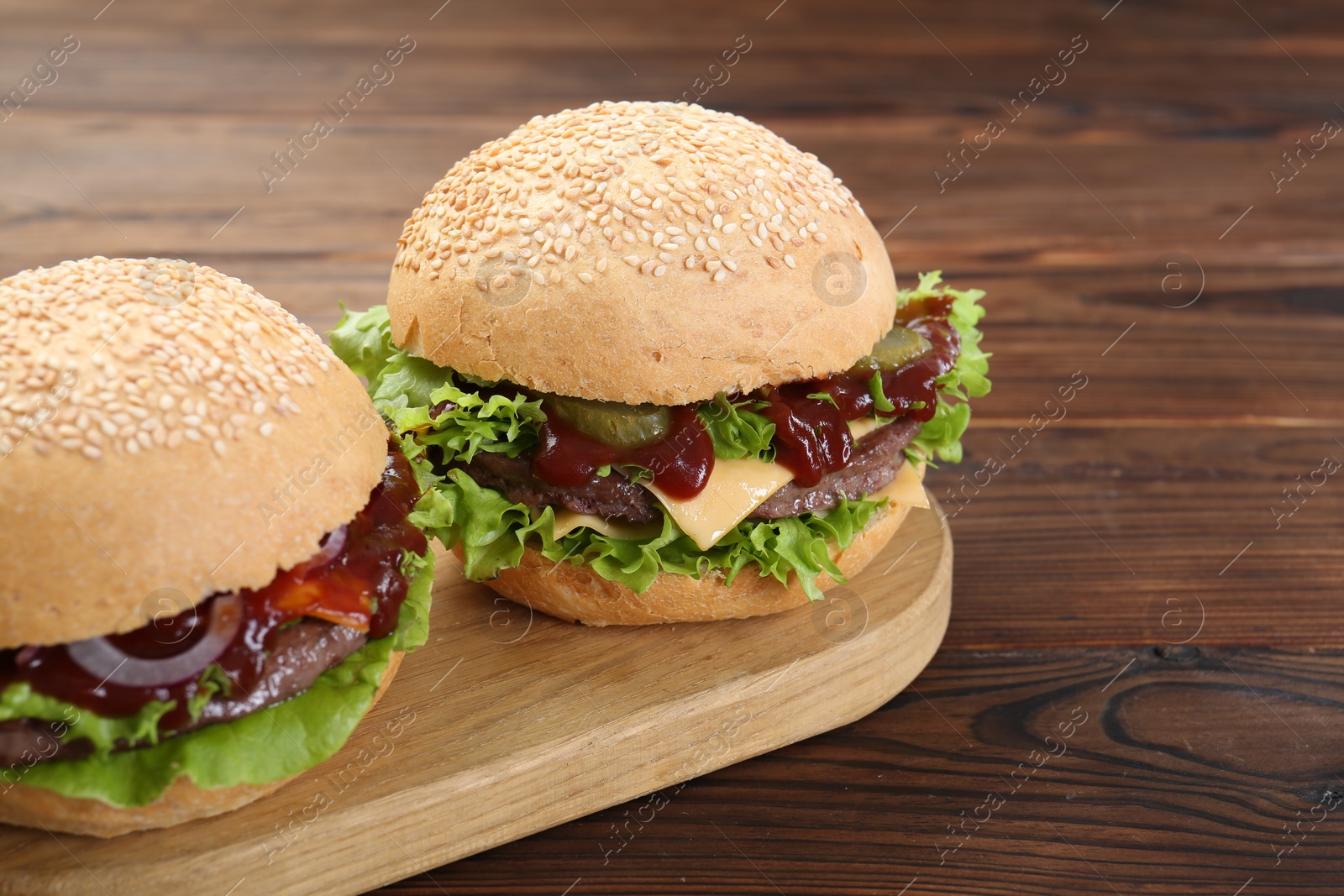 Photo of Board with delicious cheeseburgers on wooden table, closeup. Space for text