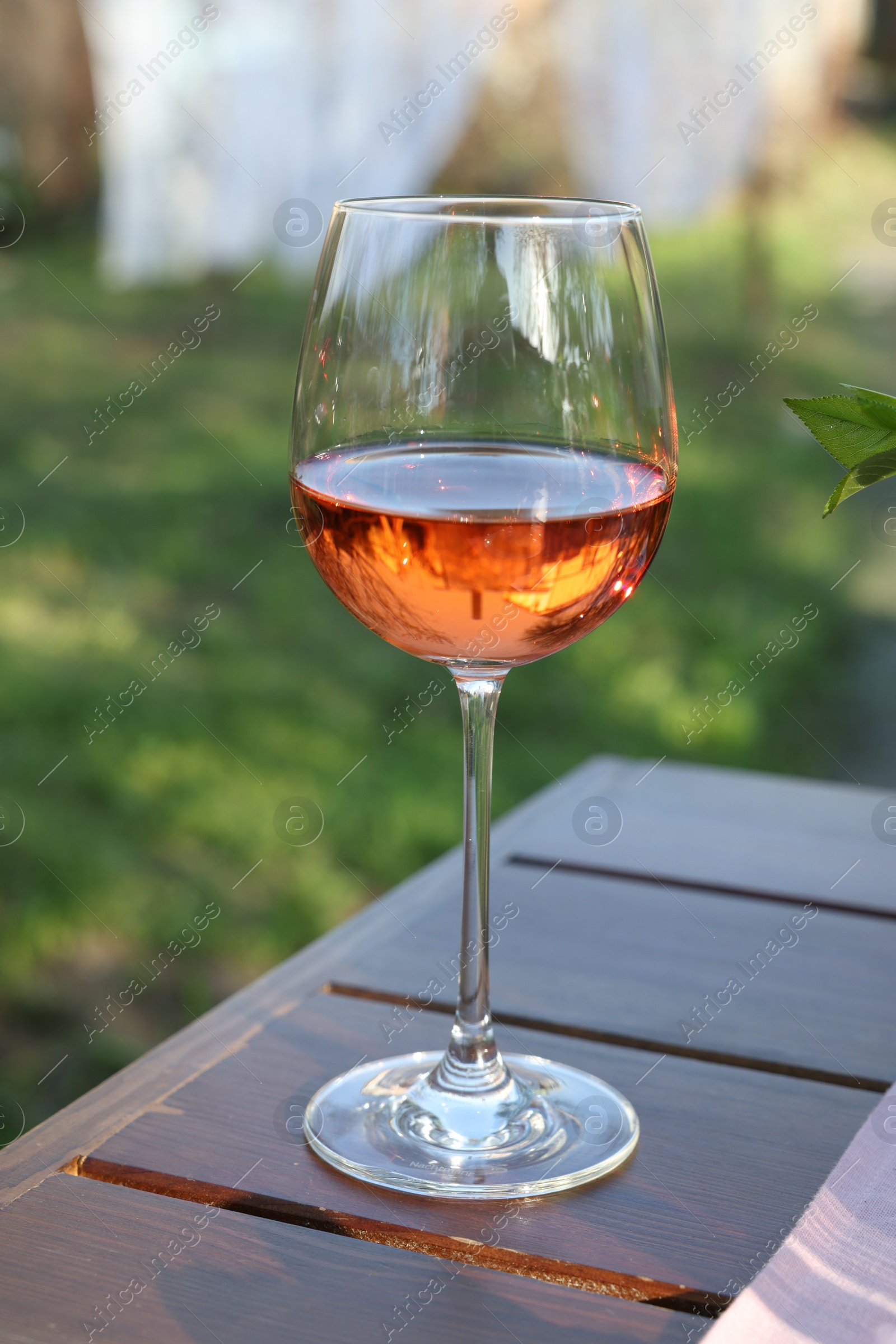 Photo of Glass of rose wine on wooden table in garden