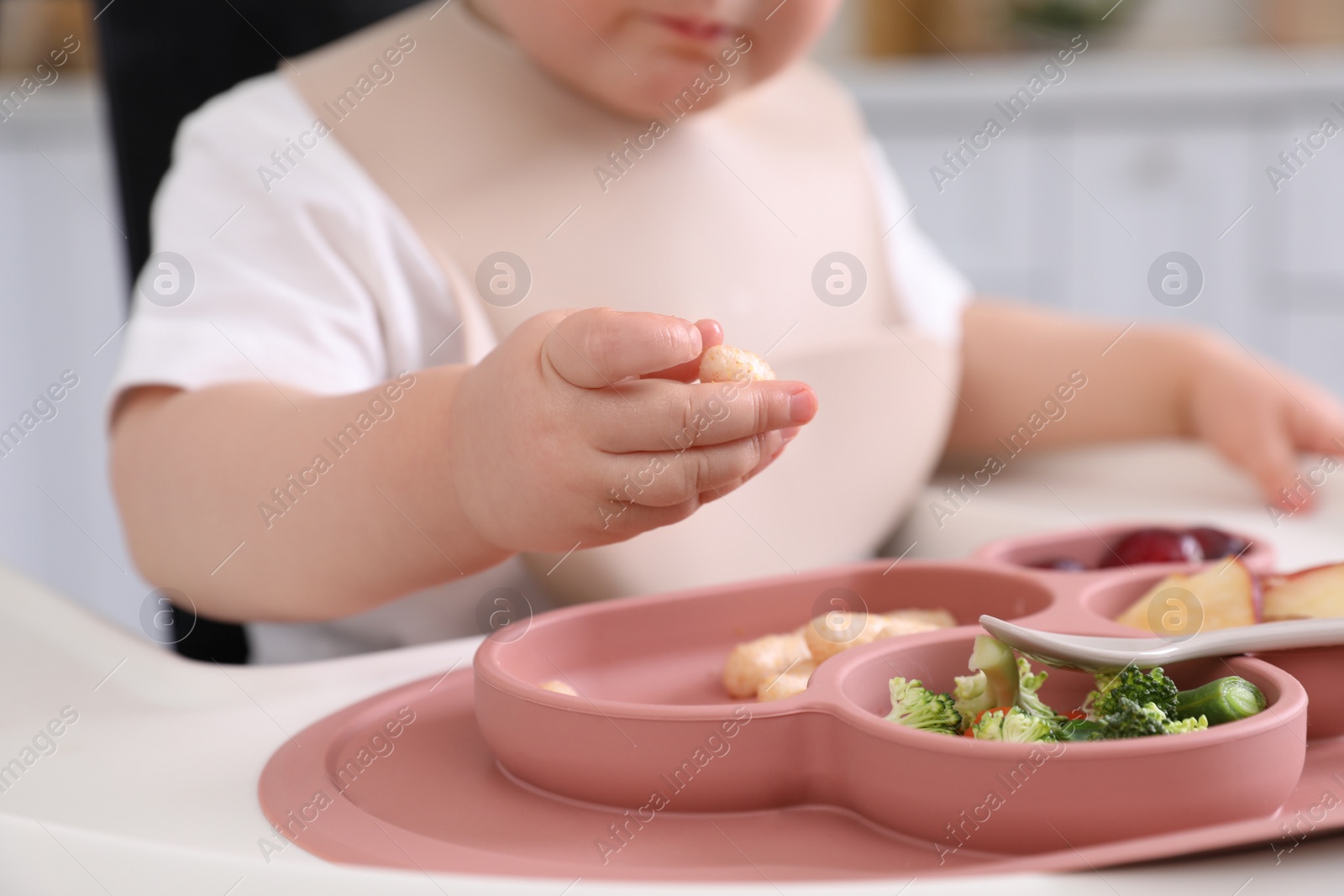 Photo of Little baby eating food in high chair at kitchen, closeup