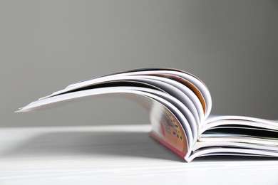 Many open magazines on white wooden table, closeup