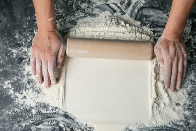 Photo of Baker rolling white flour with pin on dark table, closeup. Space for text
