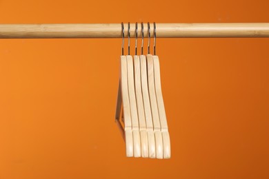 Photo of Empty clothes hangers on wooden rack against orange background