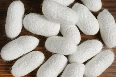 Photo of Heap of white silk cocoons on wooden table, flat lay