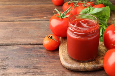 Photo of Jar of tasty ketchup and tomatoes on wooden table, closeup. Space for text