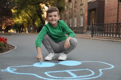 Photo of Child drawing car with chalk on asphalt