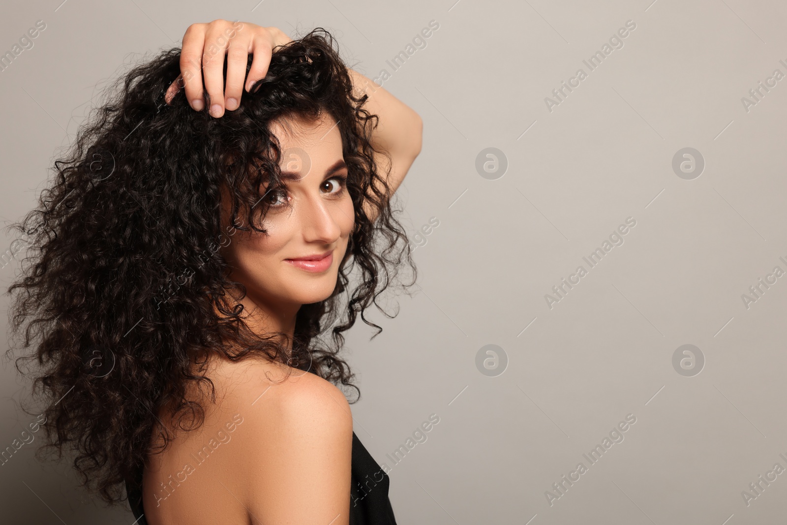 Photo of Beautiful young woman with long curly hair on light grey background. Space for text