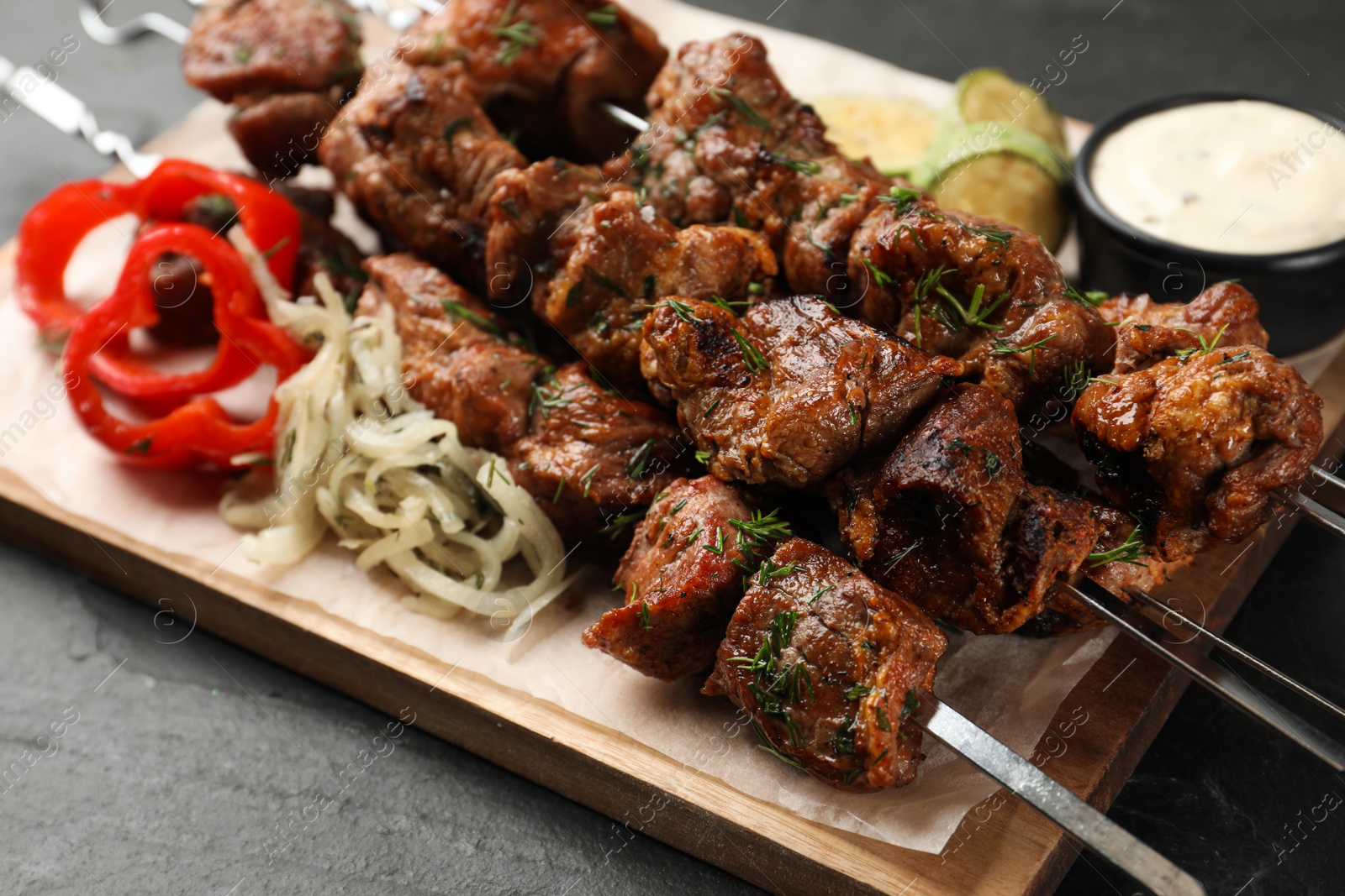 Photo of Metal skewers with delicious meat and vegetables served on black table, closeup