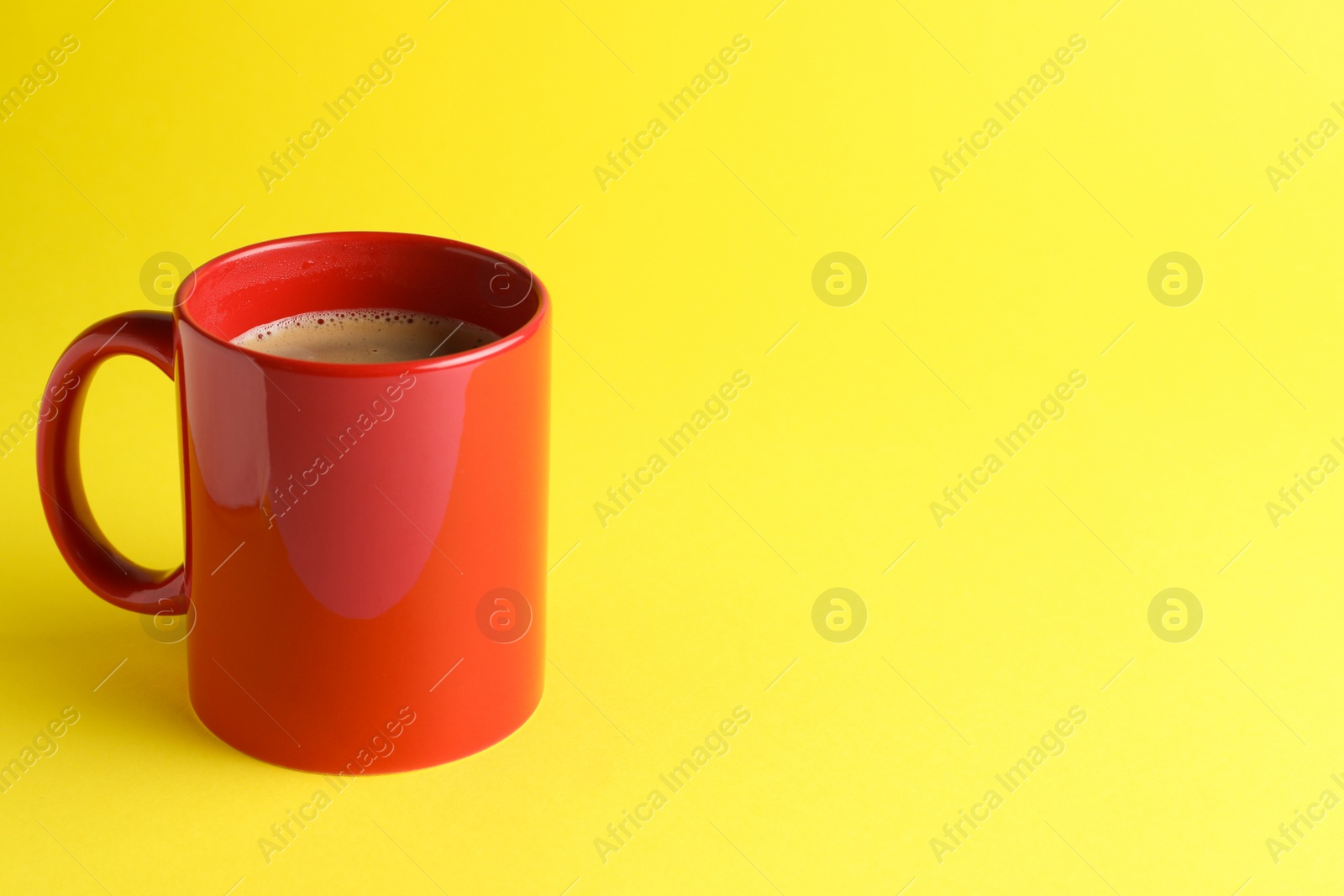 Photo of Red mug of freshly brewed hot coffee on yellow background, space for text