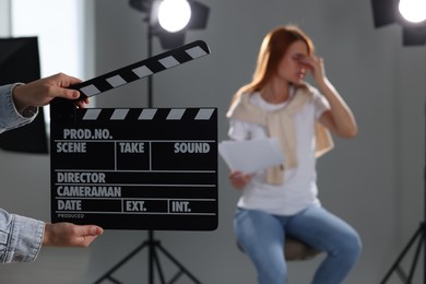 Photo of Casting call. Emotional woman performing while second assistance camera holding clapperboard against grey background in studio, selective focus