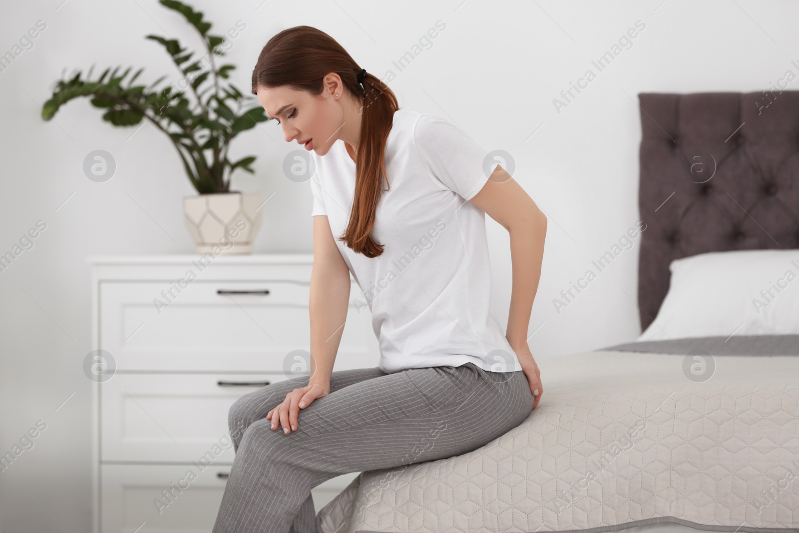 Photo of Young woman suffering from hemorrhoid on bed at home