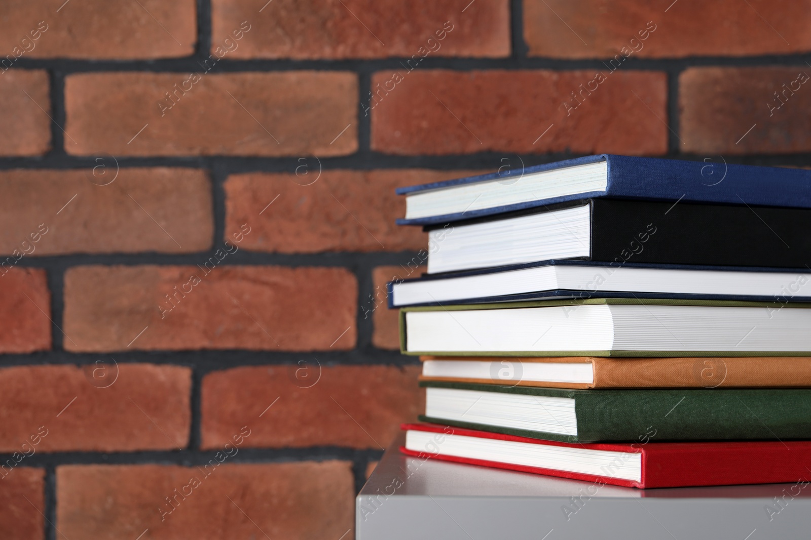 Photo of Many hardcover books on grey table near brick wall