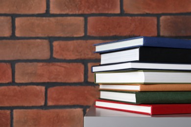 Many hardcover books on grey table near brick wall