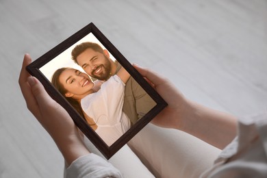 Image of Woman holding frame with photo portrait of young couple indoors, closeup