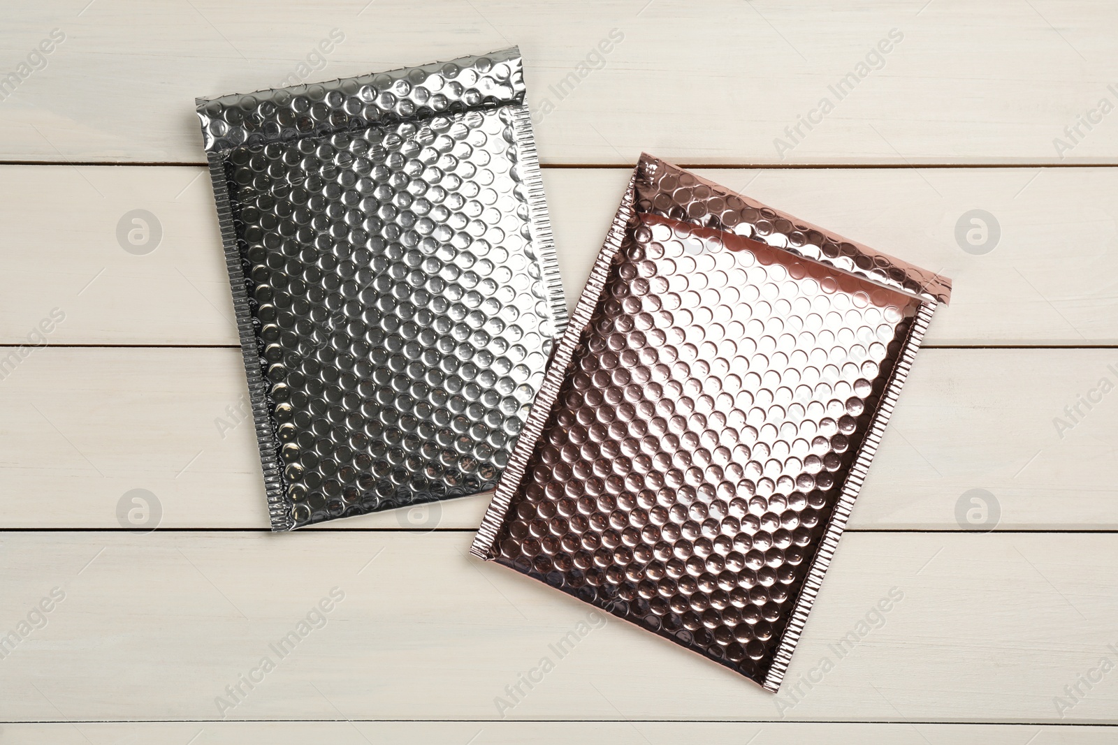 Photo of Two padded envelopes with bubble wrap on white wooden background, flat lay