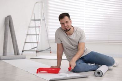 Photo of Man applying glue onto wallpaper sheet in room