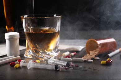 Photo of Alcohol and drug addiction. Whiskey in glass, syringes, pills and cigarettes on grey table