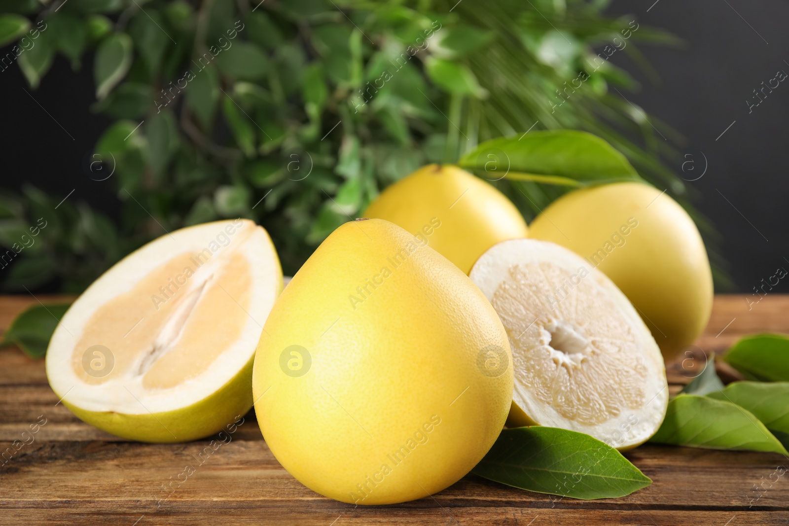 Photo of Fresh cut and whole pomelo fruits with leaves on wooden table, closeup