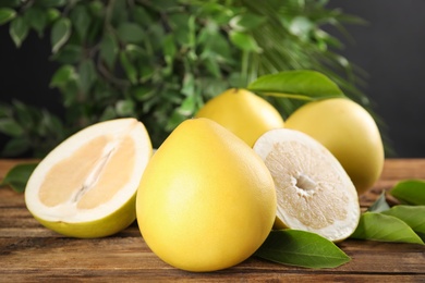 Photo of Fresh cut and whole pomelo fruits with leaves on wooden table, closeup