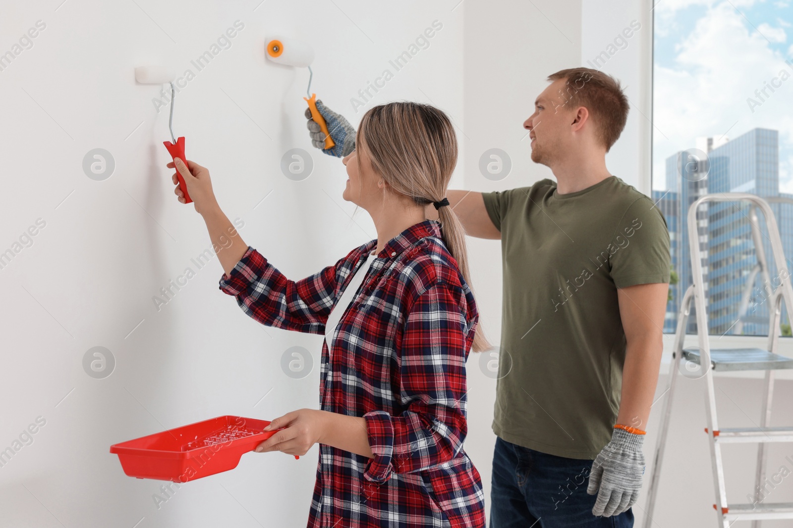 Photo of Happy couple painting wall in apartment during repair