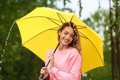 Happy young woman with bright umbrella under rain outdoors