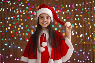 Photo of Cute little child in Santa hat on blurred lights background. Christmas celebration