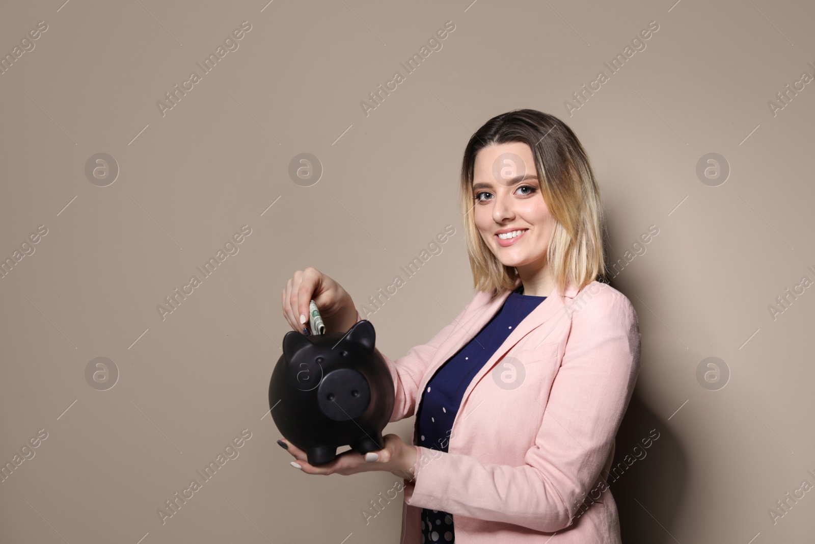 Photo of Businesswoman putting money into piggy bank on color background. Space for text