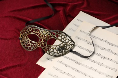 Elegant face mask and music sheets on red fabric. Theatrical performance