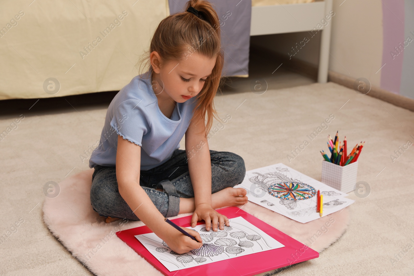 Photo of Little girl coloring antistress page on floor indoors