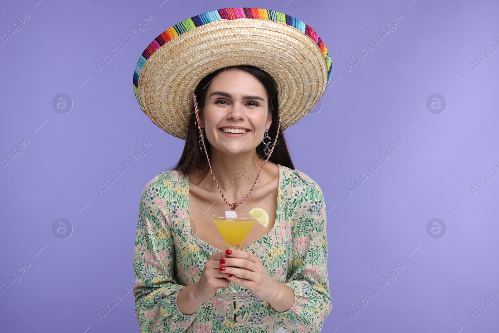 Photo of Young woman in Mexican sombrero hat with cocktail on violet background