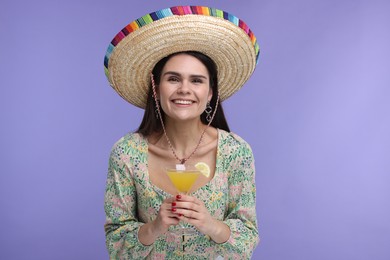 Young woman in Mexican sombrero hat with cocktail on violet background