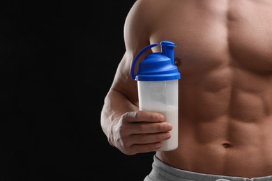 Young man with muscular body holding shaker of protein on black background, closeup. Space for text