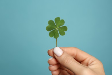 Photo of Woman holding green four leaf clover on light blue background, closeup