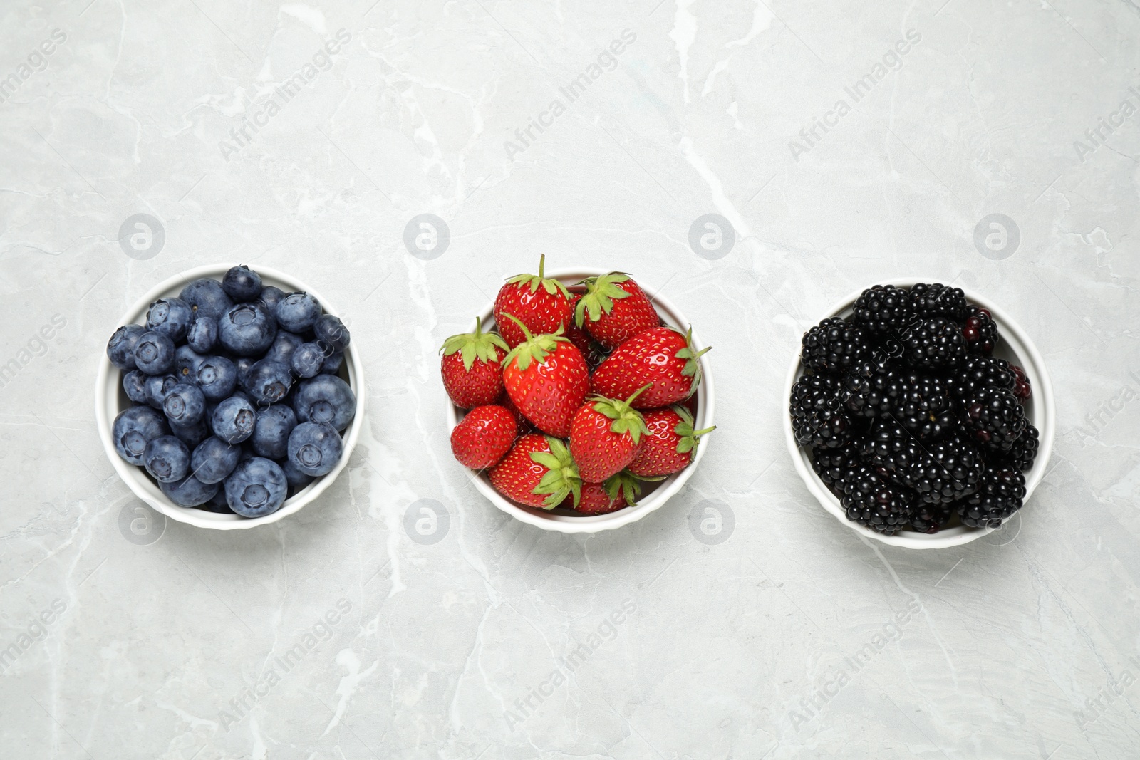 Photo of Different ripe berries on light marble table, flat lay