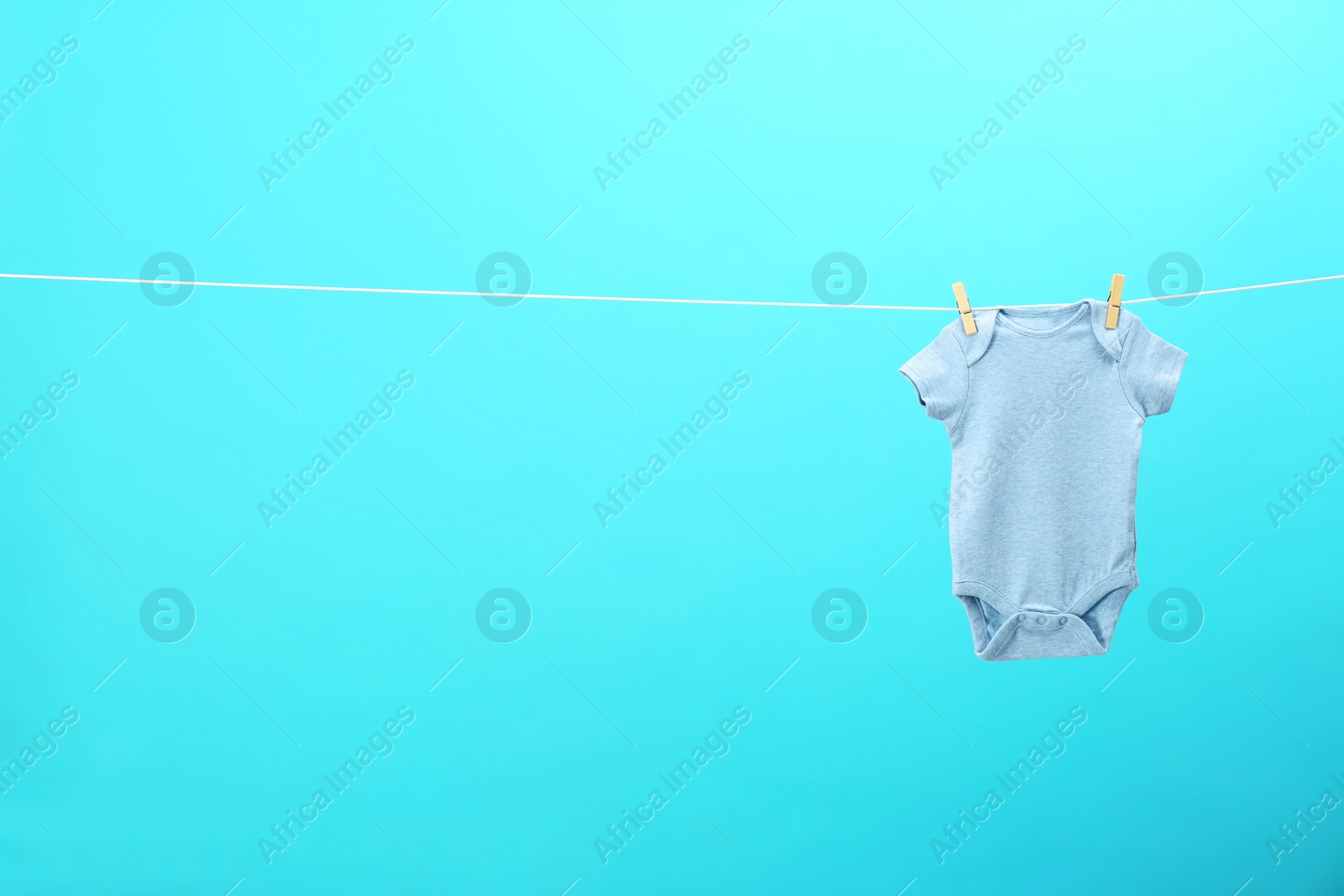 Photo of Baby onesie hanging on clothes line against blue background, space for text. Laundry day