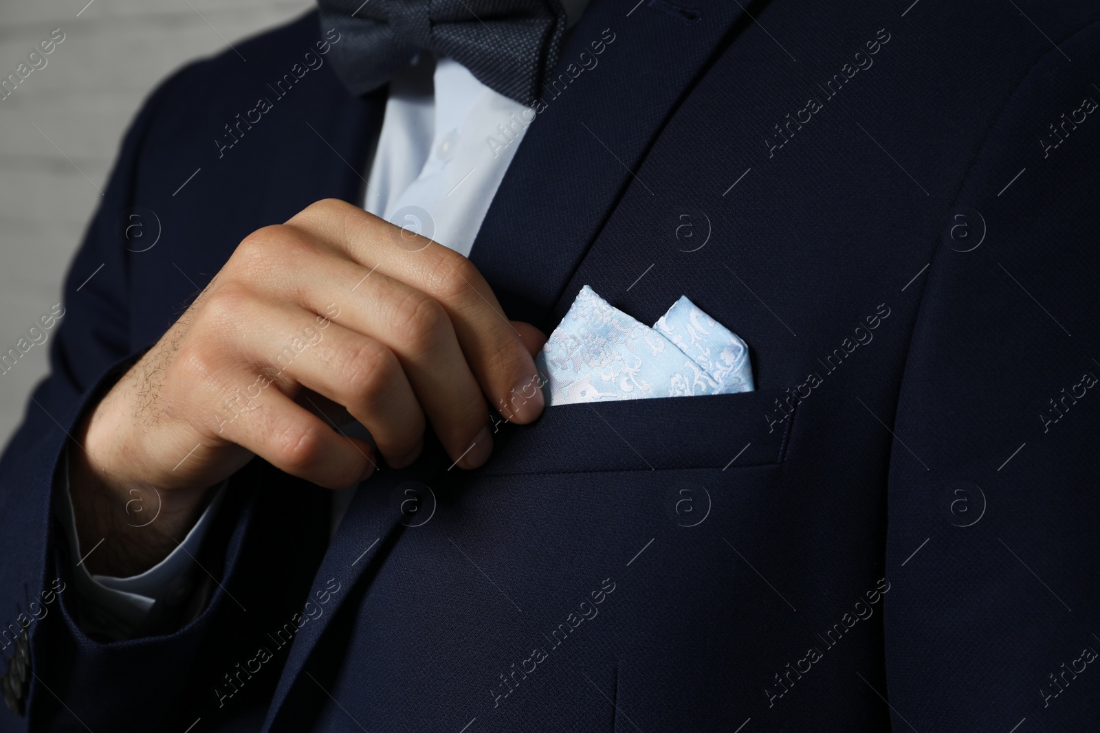 Photo of Man fixing handkerchief in breast pocket of his suit on light background, closeup