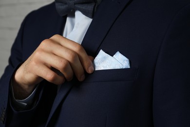 Photo of Man fixing handkerchief in breast pocket of his suit on light background, closeup